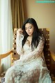 A woman in a white dress sitting on a wooden chair.