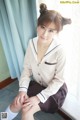 A woman in a school uniform sitting on a window sill.