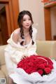 A woman sitting on a couch holding a bunch of red roses.