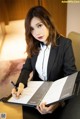 A woman in a business suit sitting at a desk with a pen and paper.