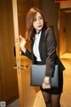 A woman in a black suit holding a black purse.