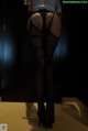 A woman in fishnet stockings and high heels standing in a dark room.