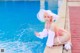 A woman in a pink bikini and a white hat sitting by a pool.