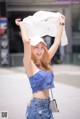 A woman in a blue top and jeans holding up a white shirt.