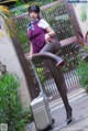 A woman in a purple uniform is posing with a suitcase.