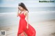 A woman in a red dress standing on a beach.