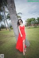 A woman in a red dress leaning against a palm tree.