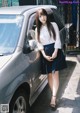 A woman standing next to a silver car on a sidewalk.