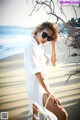 A woman in a white shirt dress and sunglasses on the beach.