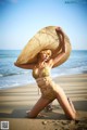 A woman in a bikini and straw hat on the beach.