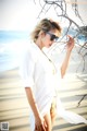 A woman in a white shirt and sunglasses standing on a beach.