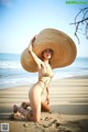 A woman in a bikini and straw hat on the beach.