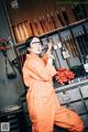 A woman in an orange jumpsuit and safety glasses in a workshop.