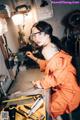 A woman in an orange jumpsuit working on a machine.