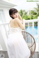 A woman in a white dress sitting on a chair by a pool.