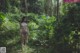 A naked woman standing in the middle of a forest.