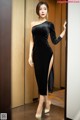 A woman in a black dress standing in an elevator.