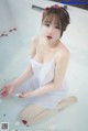 A woman in a white dress sitting in a bathtub.