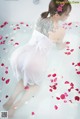 A woman in a white dress is sitting in a bathtub filled with rose petals.