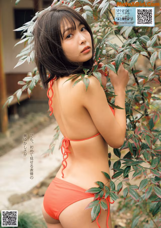 A woman in a red bikini standing next to a bush.