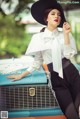 A woman in a white shirt and black hat leaning on a blue car.