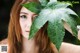 A woman holding a large green leaf over her face.