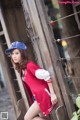 A woman leaning against a wooden fence wearing a baseball cap.