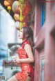 A woman in a red dress leaning against a wall.