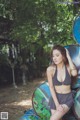 A woman in a black and white bikini sitting on a pile of blue barrels.