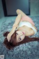 A woman laying on a gray rug with her hands on her head.