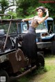 A woman in a leopard print top and black skirt leaning on an old truck.