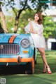 A woman in a white dress standing next to a blue car.