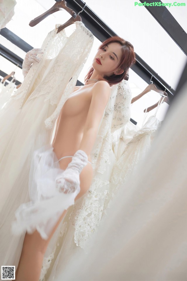 A naked woman standing in front of a rack of wedding dresses.