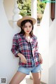 a woman wearing a hat and a plaid shirt leaning against a wall