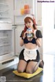 A woman in a maid outfit sitting on a pillow in front of an open refrigerator.