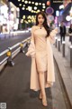 A woman in a beige dress and fur coat walking down the street.