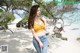 A woman in a yellow top and jeans standing on a beach.