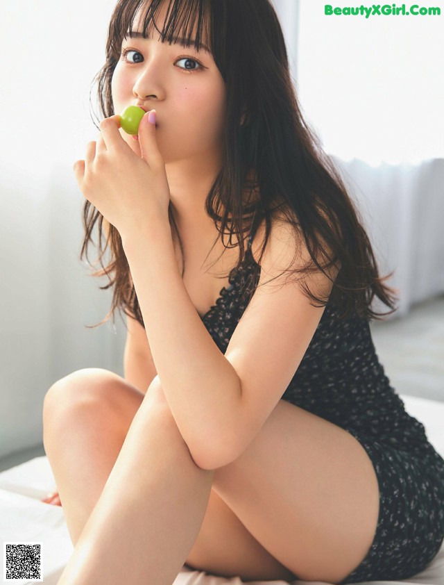 A woman sitting on a bed eating a green apple.