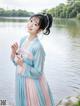 A woman in a blue and pink dress standing by a lake.