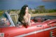 A woman sitting in the back of a red convertible car.