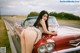 A woman leaning on the hood of a red car.