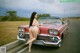 A woman leaning on the hood of a red car.