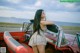 A woman leaning on the hood of a red convertible car.