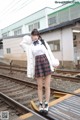 A woman in a school uniform standing on a train track.