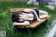 A woman laying on a wooden bench in the grass.