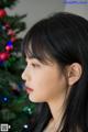 A woman with long black hair standing in front of a Christmas tree.