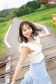 A woman in a white top and blue skirt standing on a train track.