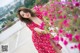 A woman in a red dress standing next to a bush of flowers.