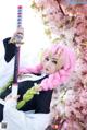 A woman with pink hair holding a sword in front of a tree.